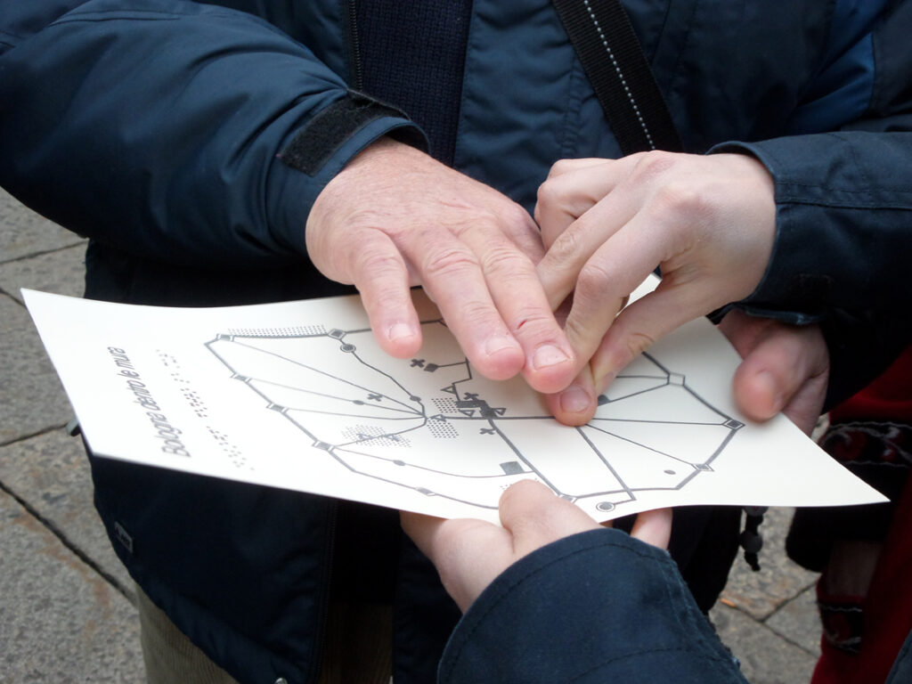 Una mano esplora una mappa tattile del centro di Bologna, guidata da un'altra mano.