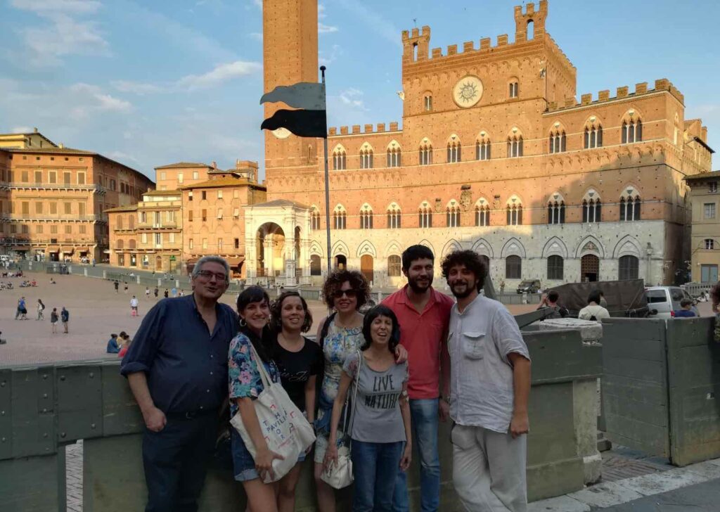 Un gruppo con accompagnatori in Piazza del Campo a Siena, nella zona della pista dei cavalli. Sullo sfondo il Palazzo Pubblico e la Torre del Mangia