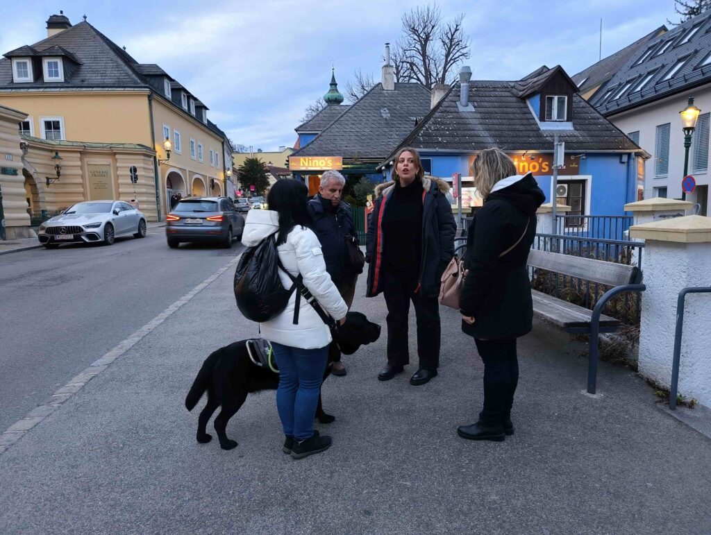 Un gruppo con cane guida ed un'accompagnatrice tra i tetti spioventi ed i lampioni del suggestivo sobborgo pedemontano di Grinzing.