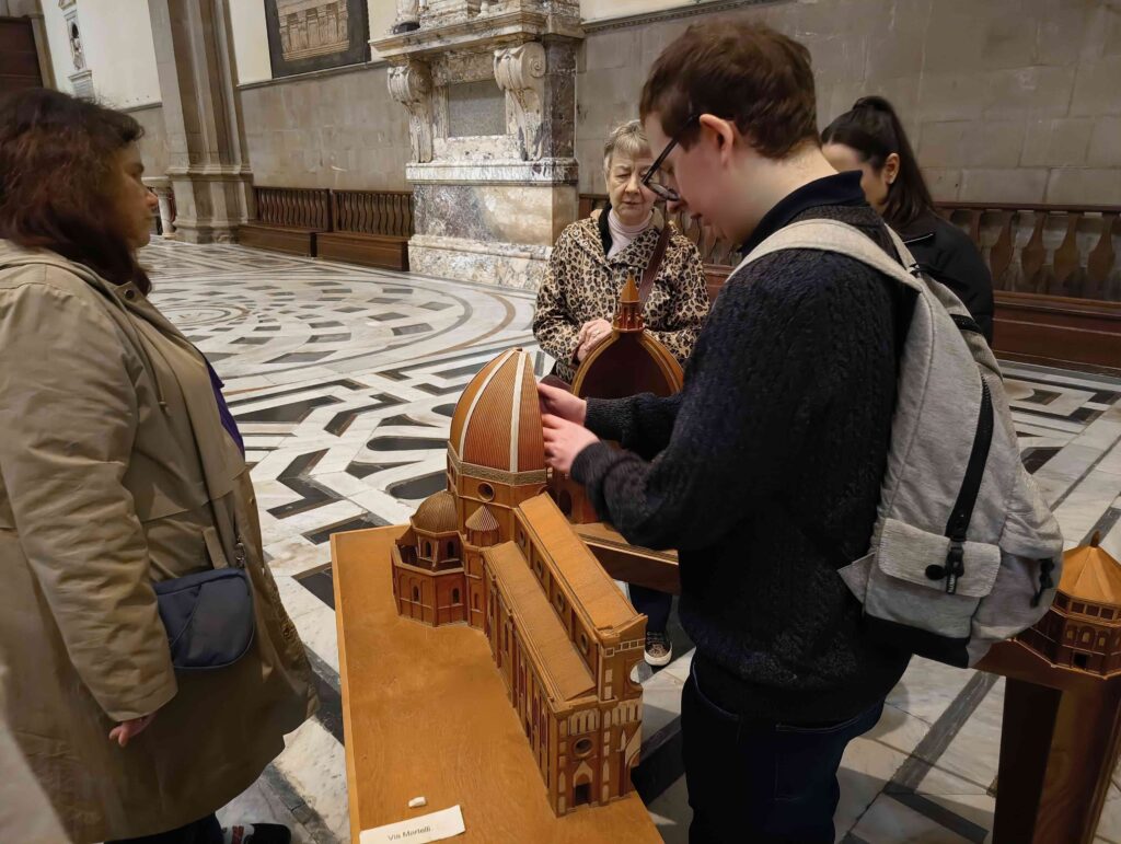 All'interno del Duomo di Santa Maria del Fiore, un viaggiatore esplora il modellino in legno del Duomo, che si può aprire lungo la navata centrale e quindi toccare anche dall'interno. Intorno a lui si vede il pavimento della navata del Duomo, ricoperto di intarsi di marmo geometrici.