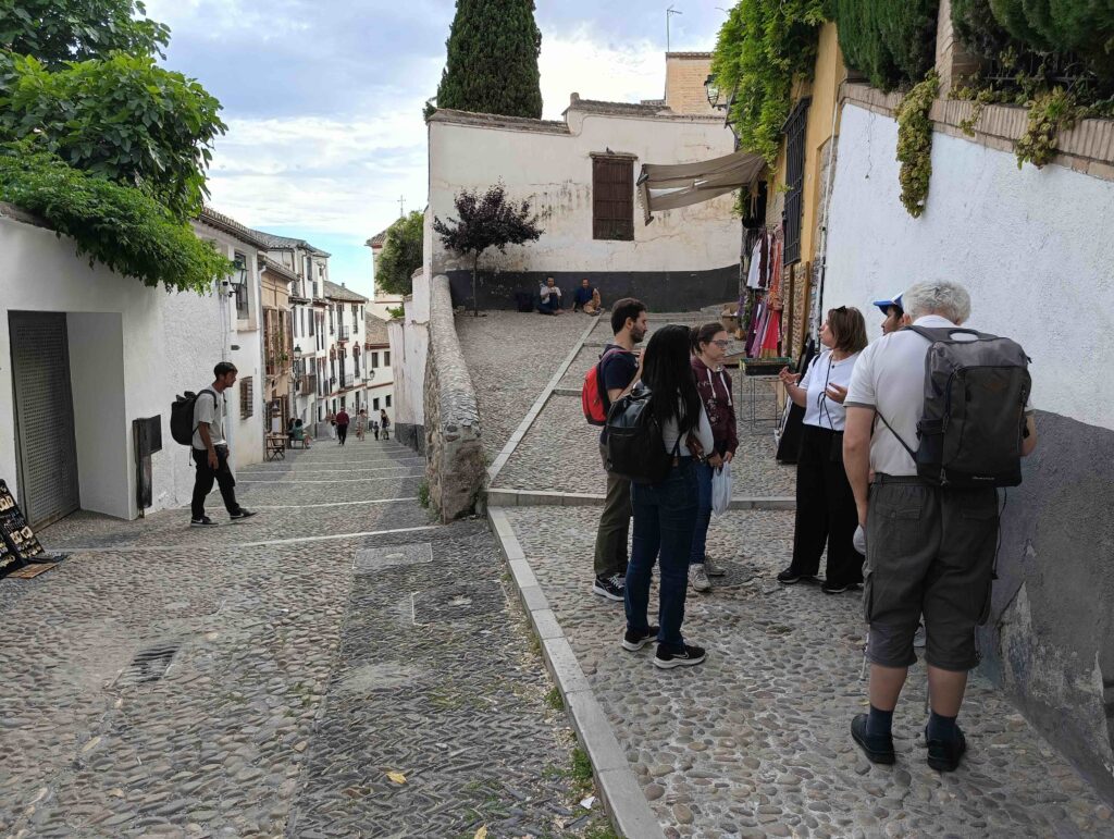 Un gruppo di viaggiatori ascolta la guida negli stretti vicoli dell'Albayzin, quartiere storico di Granada con case basse e scoscese stradine di ciottoli.