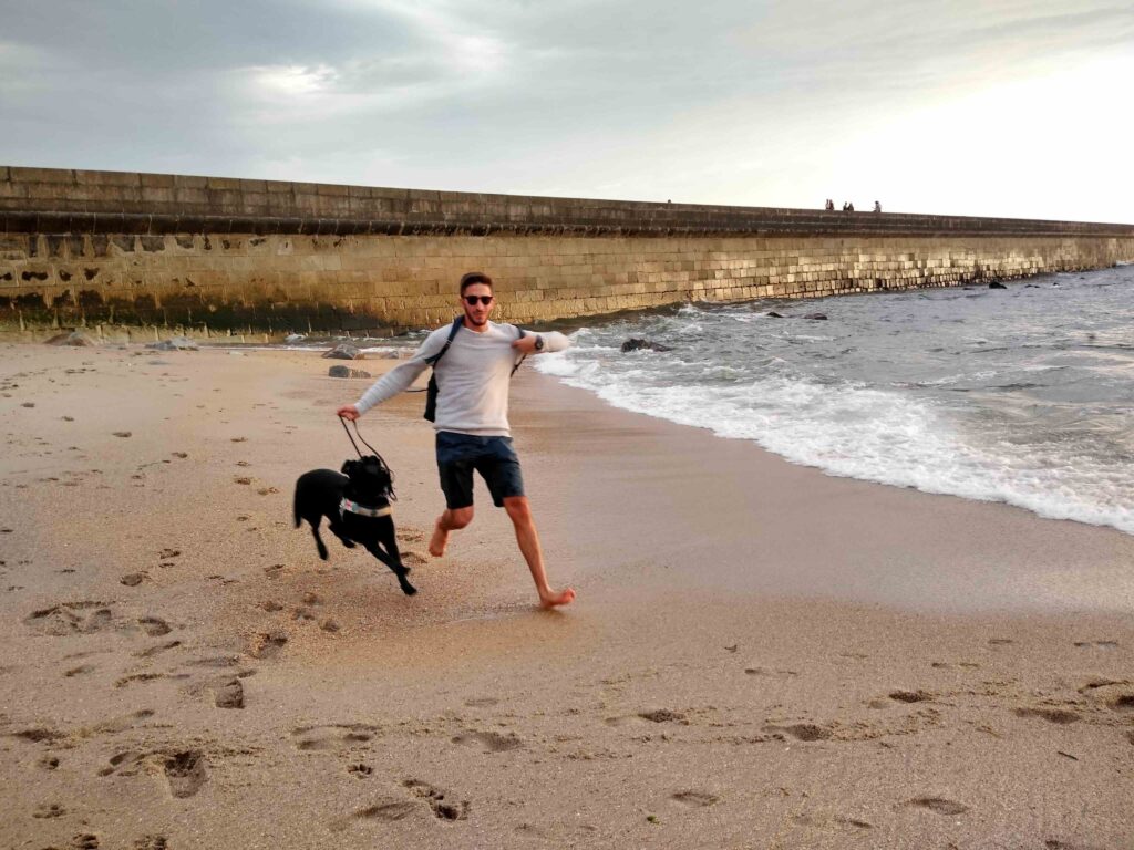 Un ragazzo ed il suo cane guida, un labrador nero, corrono su una spiaggia. Dietro di loro, un lungo frangiflutti in pietra.