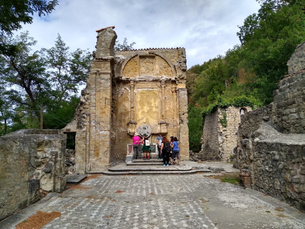 Un gruppo di camminatori, di spalle, fra le rovine a cielo aperto della chiesa di San Martino a Monte Sole, distrutta dai nazisti. Tutt'intorno ricresce la vegetazione.