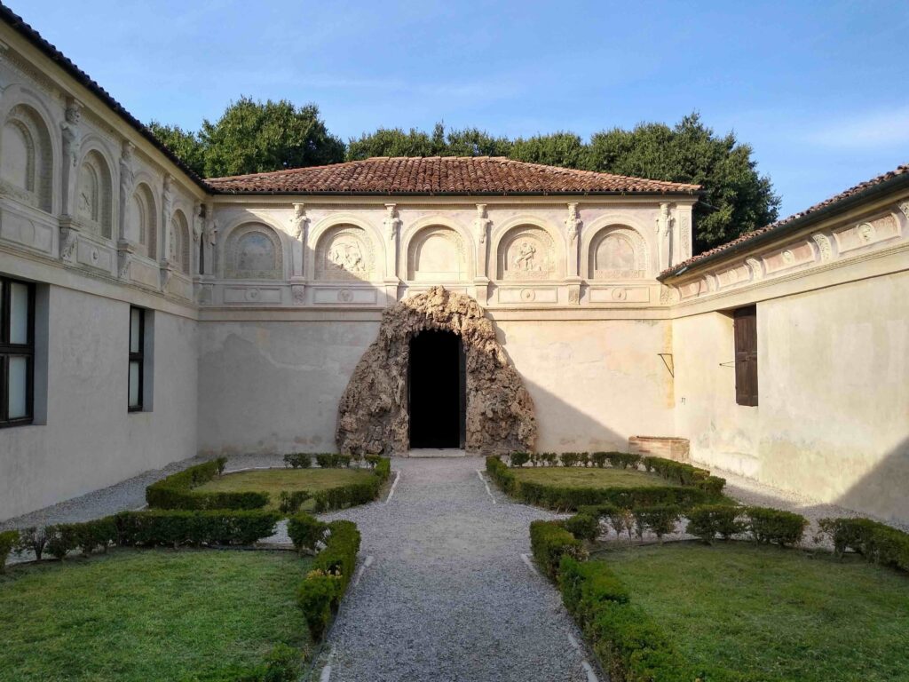 Vista del Giardino Segreto di Palazzo Te: al centro di un cortile con quattro aiuole, una porta è circondata da una composizione di rocce marine e coralli che la rendono simile ad un grottino.