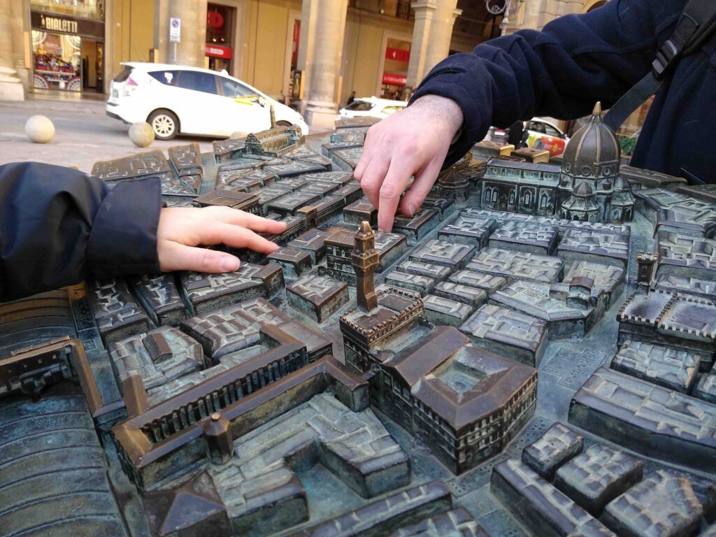 Alcune mani toccano un plastico in bronzo del centro storico di Firenze, ben riconoscibili la cupola del Duomo e la torre di Palazzo Vecchio.