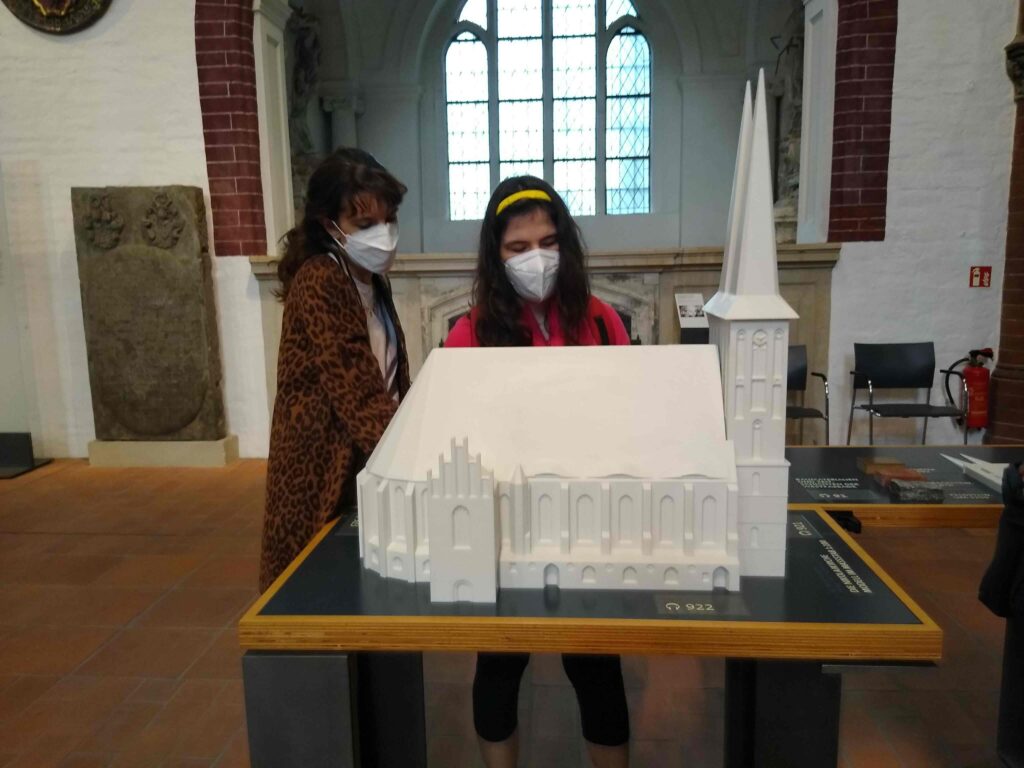 Un'accompagnatrice ed una viaggiatrice toccano un plastico della medievale Nikolaikirche a Berlino, all'interno della navata laterale della stessa chiesa.