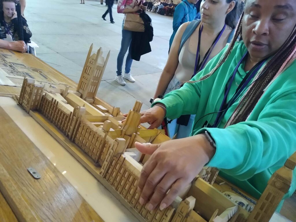 Una viaggiatrice tocca un plastico in legno del palazzo di Westminster, in primo piano con le sue numerose guglie e finestre.